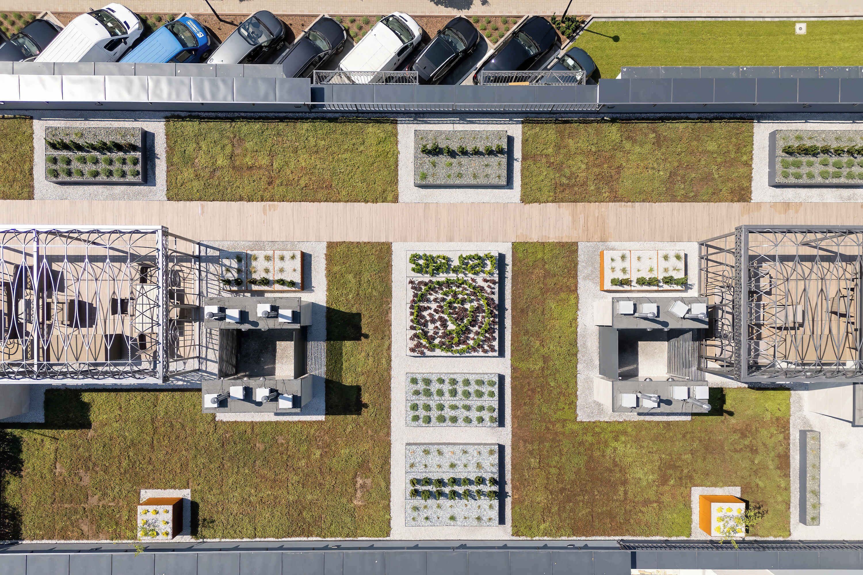 An aerial view of a parking lot with multiple rows of parked cars, a green lawn area, and a building with a rooftop garden.