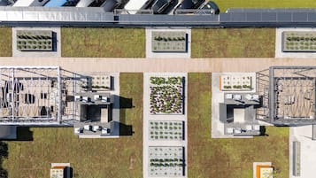 An aerial view of a parking lot with multiple rows of parked cars, a green lawn area, and a building with a rooftop garden.