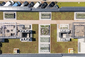 An aerial view of a parking lot with multiple rows of parked cars, a green lawn area, and a building with a rooftop garden.