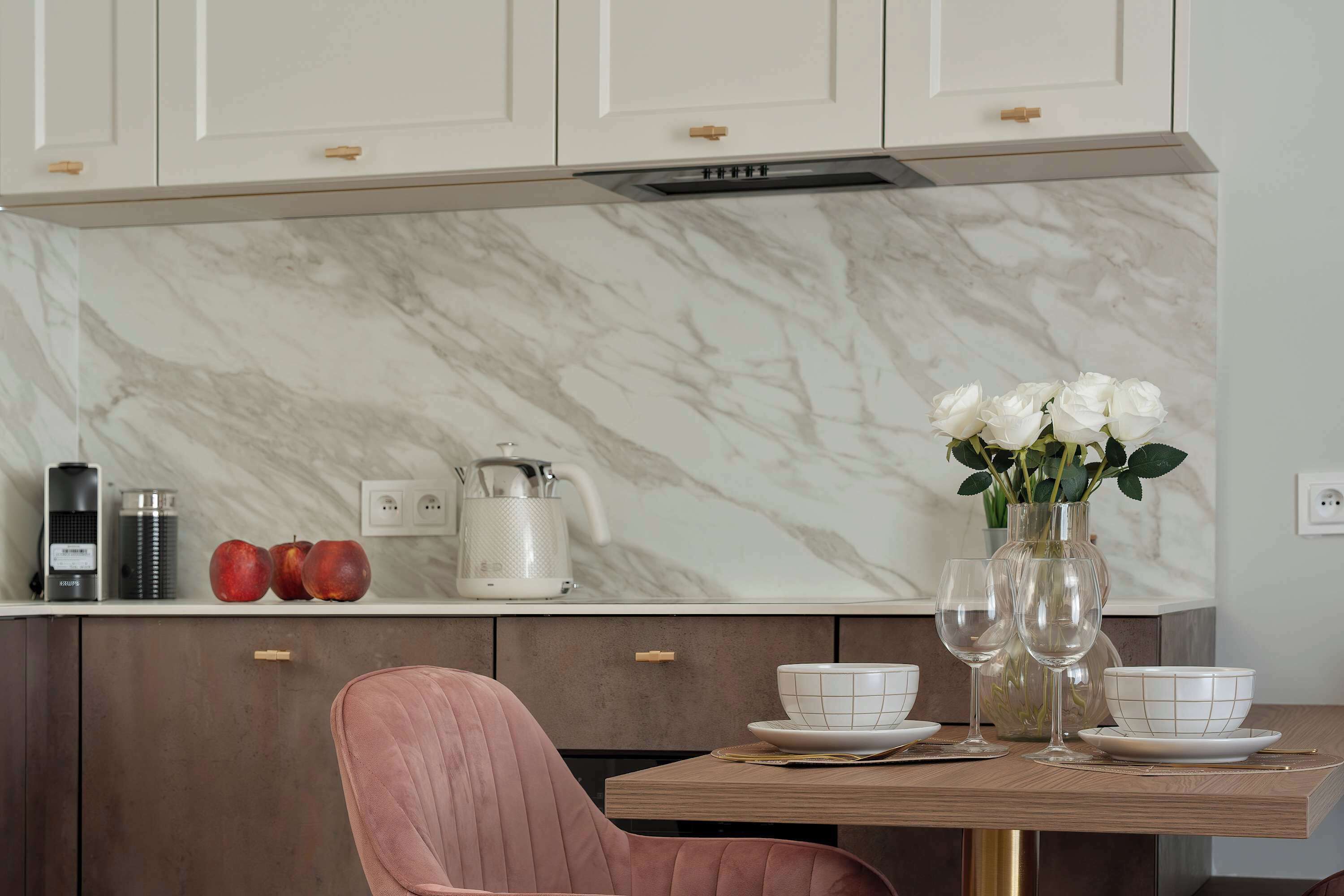 Een moderne keuken met een marmeren spatwand, een eettafel met witte borden en een roze stoel.
