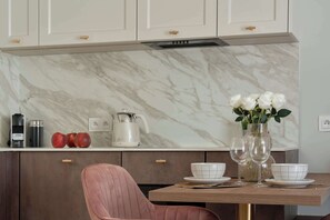 Una cuina moderna amb frontissa de marbre, taula de dinar amb plats blancs i una cadira rosa.