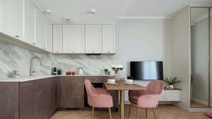 A modern kitchen with marble backsplash, white cabinets, and a dining area with pink chairs and a round table.