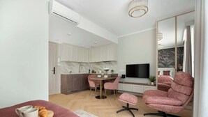 Un dormitorio moderno con cama, un sillón rosa, un televisor y una zona de cocina con encimera de mármol.