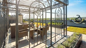 A covered outdoor seating area with wicker furniture and a table, surrounded by a metal fence with decorative patterns.