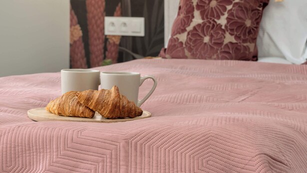 A bed with a pink blanket, a floral pillow, and a wall with a plant mural.