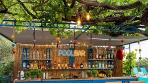 Un bar a bordo piscina all'aperto con design blu e in legno, che mostra una varietà di bottiglie e un lampadario.