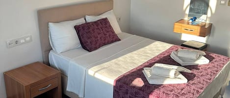 A single bed with a headboard, a bedside table, a nightstand, a mirror, and a wall socket.
