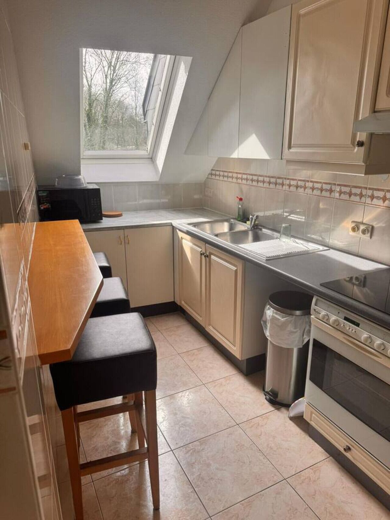 Een kleine keuken met een raam, een magnetron, een spoelbak en een fornuis.