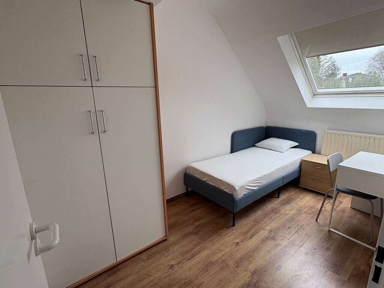 Ein kleines Zimmer mit einem Bett, einem Schreibtisch und einem Kleiderschrank.