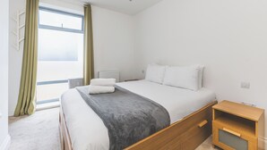Ein Schlafzimmer mit einem Bett, einem Nachttisch, einem Heizkörper und einem Fenster mit Vorhängen.