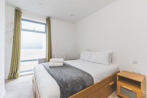 Ein Schlafzimmer mit einem Bett, einem Nachttisch, einem Heizkörper und einem Fenster mit Vorhängen.