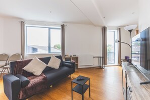 Ein modernes Wohnzimmer mit einem dunklen Sofa, einem kleinen schwarzen Tisch und einem großen Fenster.