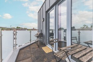 Ein Balkon mit Grill, einer Bank und einer Tür zu einem Innenraum.