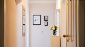 Ein Flur mit gerahmten Bildern an der Wand, einer Tür rechts und einem Schrank mit einer Blumenvase.
