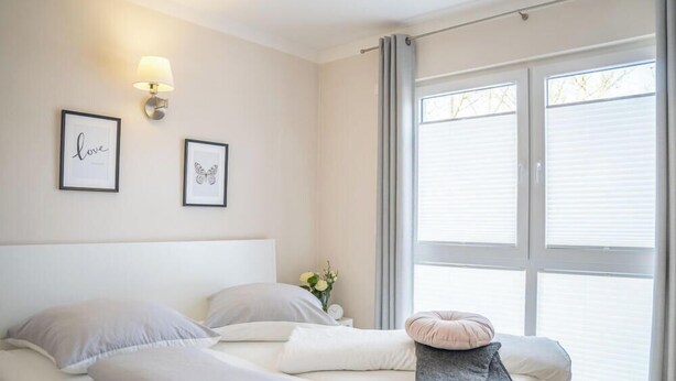 Ein Schlafzimmer mit einem Bett, Kissen, einem Nachttisch mit Lampe und einem Fenster mit Jalousien.