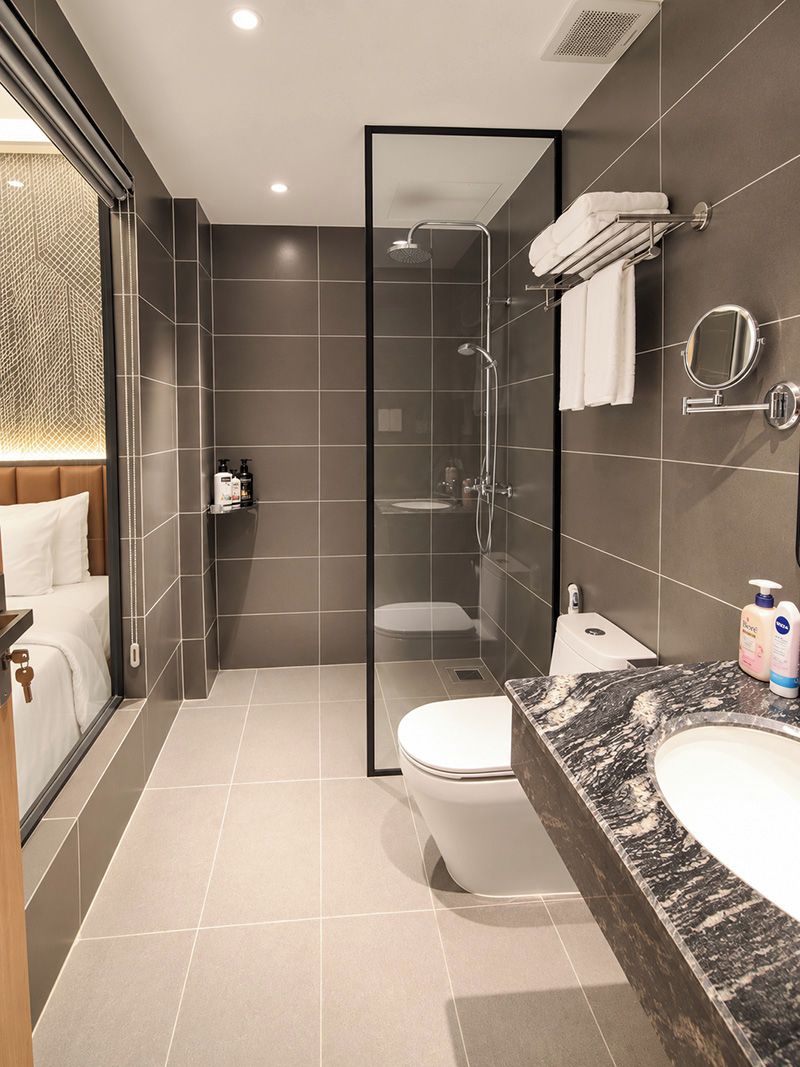Une salle de bain moderne avec une douche à l’italienne en verre, des toilettes blanches, un lavabo en marbre et une table de chevet avec une serviette blanche.