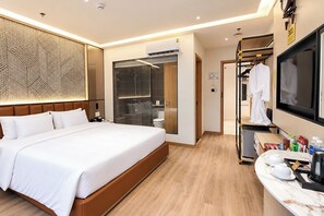 Une chambre d’hôtel moderne dotée d’un grand lit, d’une salle de bain avec une porte en verre, d’une télévision et d’un comptoir avec des articles de toilette.