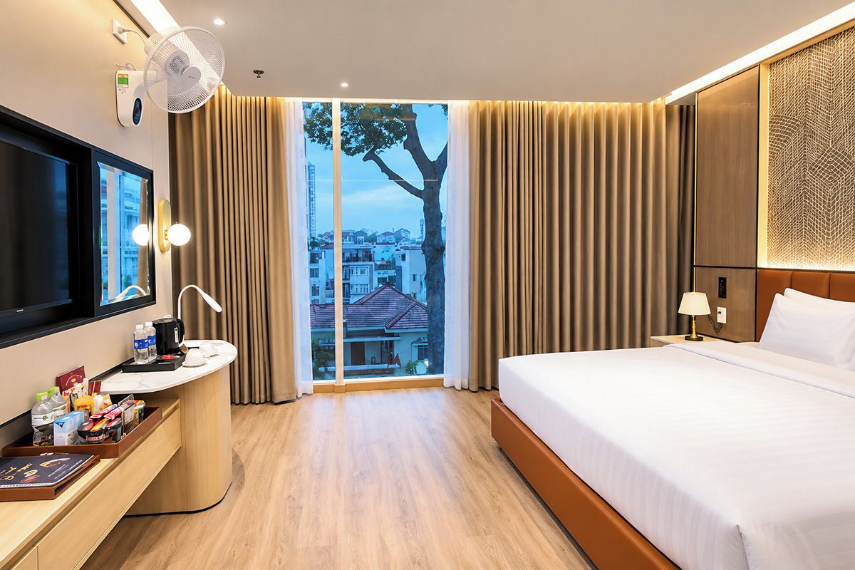 Habitación de hotel con cama, escritorio con espejo, televisión y ventana con cortinas.