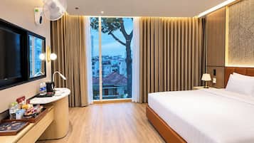 A hotel room with a bed, a desk with a mirror, a TV, and a window with curtains.