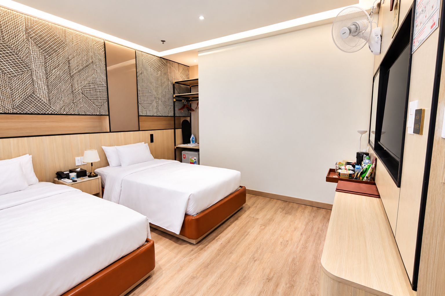 A hotel room with two beds, a TV, a wardrobe, and a desk with a lamp.