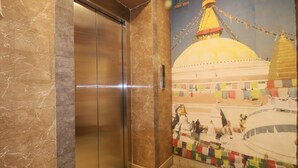 A marble elevator door with a mural of a temple and prayer flags.