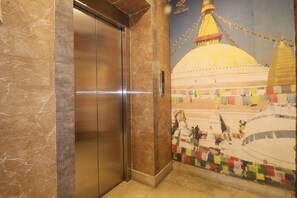 A marble elevator door with a mural of a temple and prayer flags.