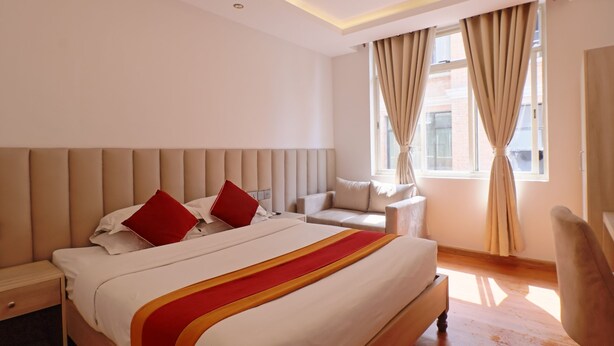 A hotel room with a large bed, a bedside table, a chair, and a window with curtains.