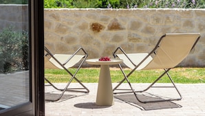 Un patio con dos sillas y una mesa, un muro de piedra y vistas a zonas verdes.