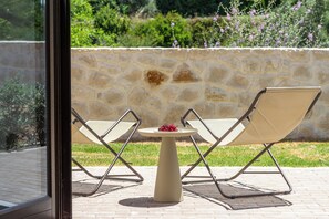 Eine Terrasse mit zwei Stühlen, einem Tisch, einer Steinsäule und Blick ins Grüne.