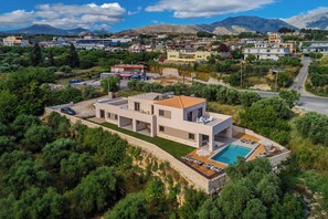 A modern two-story house with a swimming pool, surrounded by greenery and a mountain in the background. - VaMa Luxury Living-8BR Design Villa with Heated Pool and Playroom (Episkopi Rethymnou)
