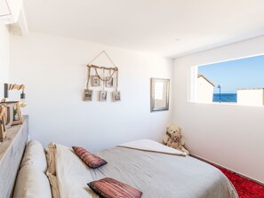 A bedroom with a bed, pillows, a teddy bear, a wall-mounted picture frame, and a window with a view of the sea. - Superbe villa contemporaine by Interhome (Hyères)