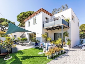 Une maison moderne à deux étages, dotée d’un balcon, d’une terrasse avec mobilier d’extérieur et d’une pelouse bien entretenue.