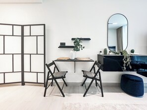 A modern room with a black-framed partition, a black sofa, a white table with a woven placemat, a mirror, and a blue ottoman. - Modern Studio with Private Jacuzzi (Dubai)