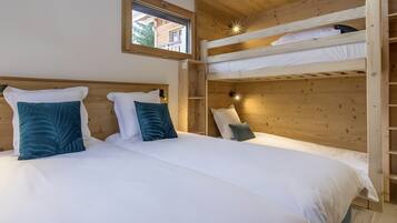 Une chambre avec un lit superposé, deux lits simples, une fenêtre et des murs en bois.