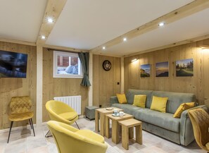 Una habitación acogedora con techo de madera, un sofá con cojines amarillos, un sillón amarillo y una pequeña mesa de madera.