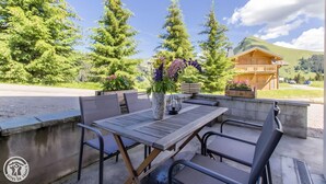 Et udendørs opholdsområde med et bord, stole, en potteplante og udsigt til et bjerg og en bygning i baggrunden.