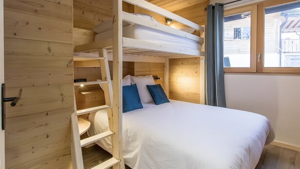 Et soveværelse med køjeseng, en stige, et vindue med gardiner og en loftlampe.