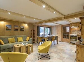 Un interior acogedor con zona de comedor de madera, un sofá con cojines amarillos y una cocina con armarios de madera.