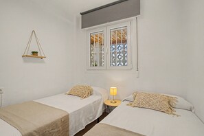 A bedroom with two single beds, a bedside table with a lamp, a hanging plant, and a window with decorative lattice. - Central Apartment 'Apto Anabel Nerja' (Nerja)