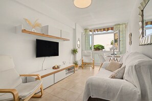A modern living room with a flat-screen TV, a sofa, a dining area with a table and chairs, and a view through a large window. - Central Apartment 'Apto Anabel Nerja' (Nerja)