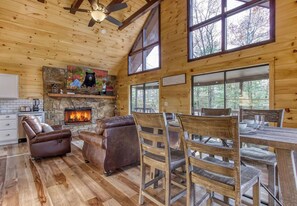 Ein Holzblockhaus-Interieur mit Kamin, Ledersesseln, einem Esstisch mit Stühlen und großen Fenstern.