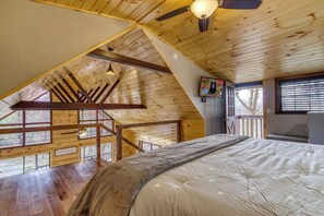 Ein Schlafzimmer mit schrägverdeckter Decke, Holzbalken, einem Bett, einem Deckenventilator und einem Fenster mit Jalousien.