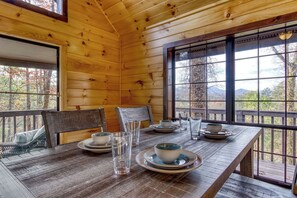 A wooden cabin interior with a dining table set for four, large windows, and a view of the outdoors. - Baby Bear-Get $560 worth of FREE area attraction tickets for each paid day!!! (Sevierville)