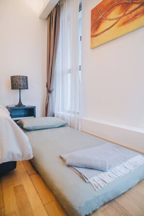 Quarto com cama, mesa de cabeceira, luminária e janela com cortinas.