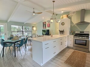 A modern kitchen with a large island, white cabinetry, a built-in oven, and a dining area with a table and chairs. - Garden Oasis Retreat — Your Private Sarasota Escape (Sarasota)