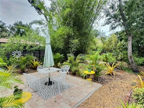An outdoor patio with a table and chairs, surrounded by lush greenery and trees. - Garden Oasis Retreat — Your Private Sarasota Escape (Sarasota)