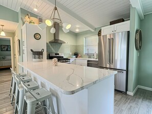 A modern kitchen with a marble island, stainless steel appliances, and a dining area with bar stools. - Garden Oasis Retreat — Your Private Sarasota Escape (Sarasota)