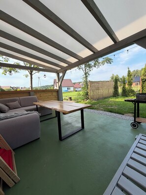 Un patio al aire libre con una mesa de madera, un sofá y un carrito para parrillada.