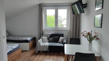 A bedroom with a bed, a sofa, a desk, a chair, a TV, and a window with curtains.