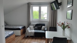 Quarto com cama, sofá, escrivaninha, cadeira, televisão e janela com cortinas.